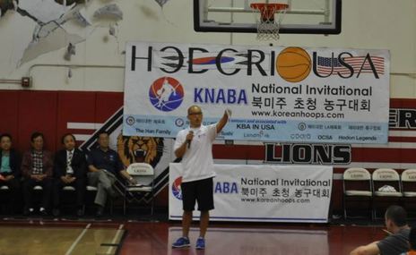 A speaker addresses players and guests in front of a KNABA National Invitational banner at an early tournament.
